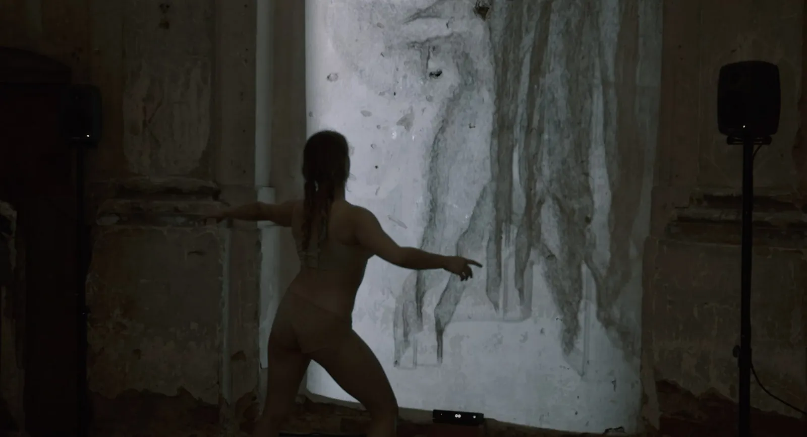 A dancer silhouetted against a large projected wall in a darkened room.